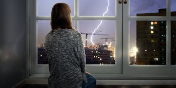Junge Frau sitzt vor Fenster, Blitz schlägt draussen ein
