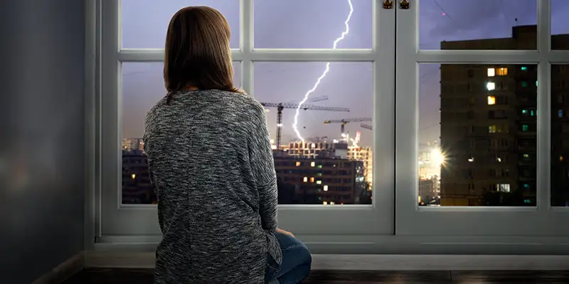 Junge Frau sitzt vor Fenster, Blitz schlägt draussen ein